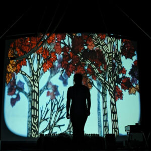 A backlit cut-paper autumn forest scene with a silhouetted figure