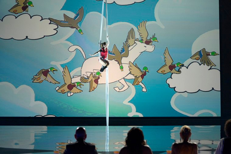 Abigail Baird suspended in aerial silks in front of a hand-drawn animated sky